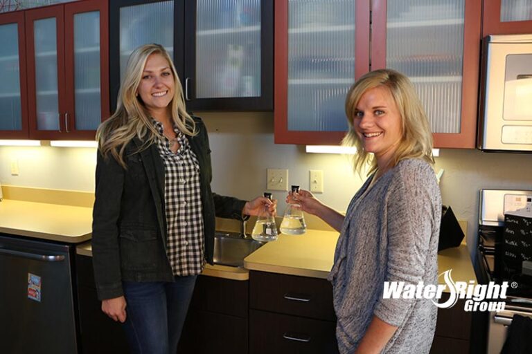 Women in kitchen holding beakers full of water