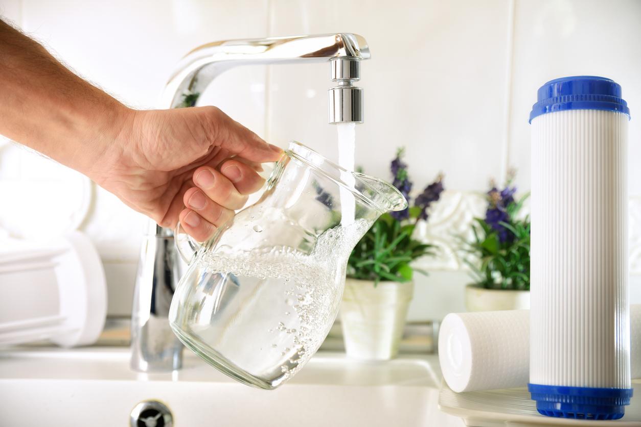 A person filling up a glass pitcher with treated water from a kitchen faucet, and a clean water filter is sitting beside the sink.