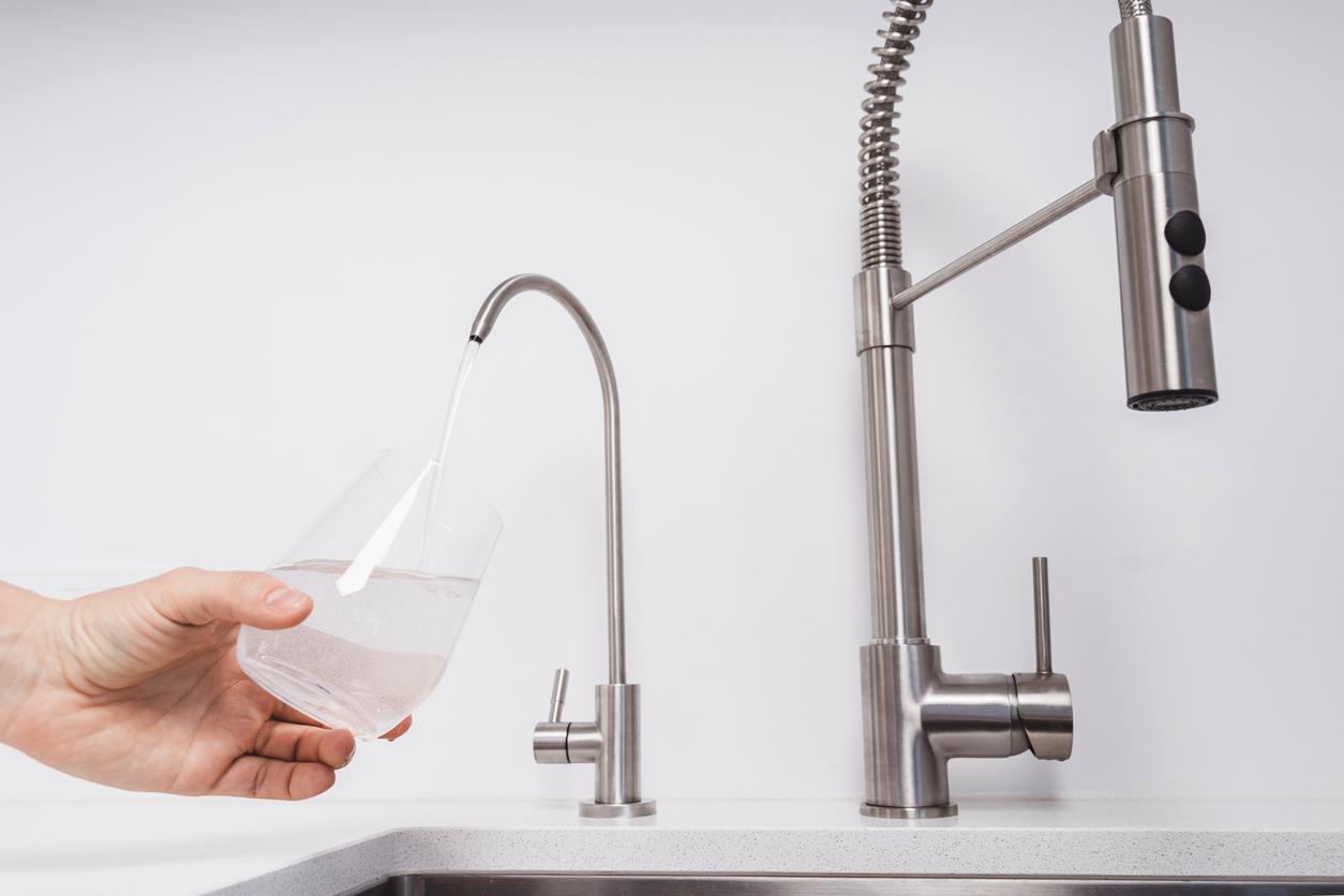 A person filling a glass with RO water from a separate faucet at a kitchen sink that is attached to a reverse osmosis system.